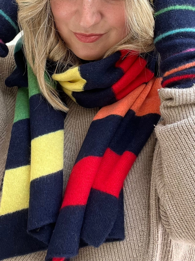 Knitted navy wristwarmers with multi coloured stripes shown worn with matching scarf