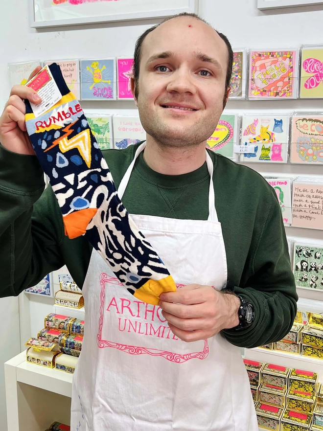 Happy artist holding 100% Organic charity cotton Rumble Socks in blue & yellow