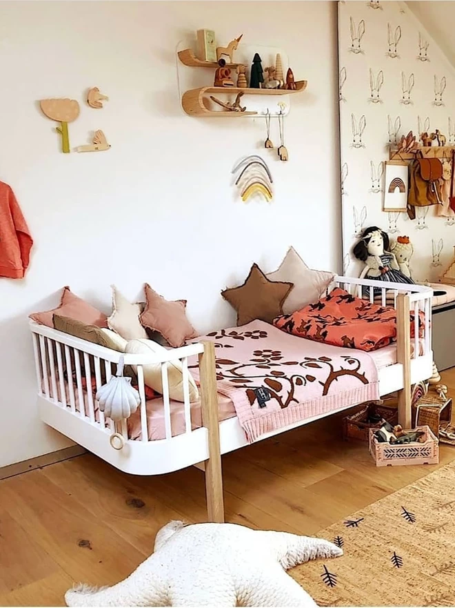 A bright and modern childrens room showing the blush briar rose junior blanket folded in half and draped across a single bed. Complimentary wall decor and accessories frame the bed creating a cosy and inviting atmosphere.