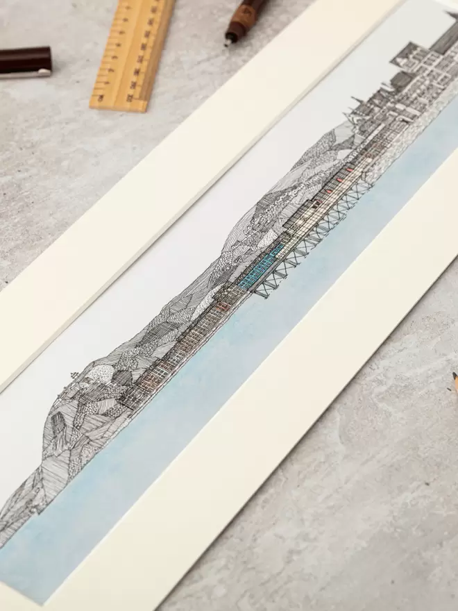 Print of detailed pen and watercolour drawing of Aberystwyth pier and seafront, with mountain backdrop, in a soft white mount