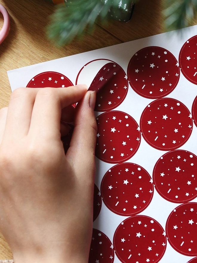 A hand is peeling a red sticker with a star pattern from a sheet of 35 matching stickers.