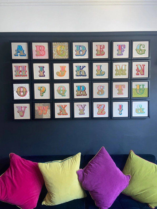 An embroidered alphabet in box frames on a wall above a sofa
