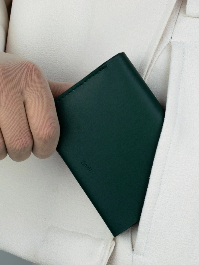 Darl Green Bifold Wallet held in hand being packed into pocket of ivory trousers
