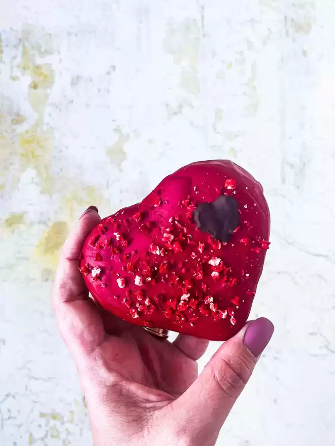 a hand holding a large red heart shaped macaron