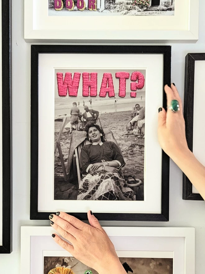 B&W photo print of woman with pink embroidered ‘What?”’ framed  held on wall
