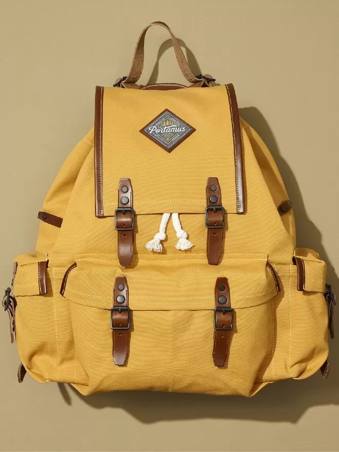 Yellow Rockness backpack with brown trim and black hardware shown in plain taupe background.