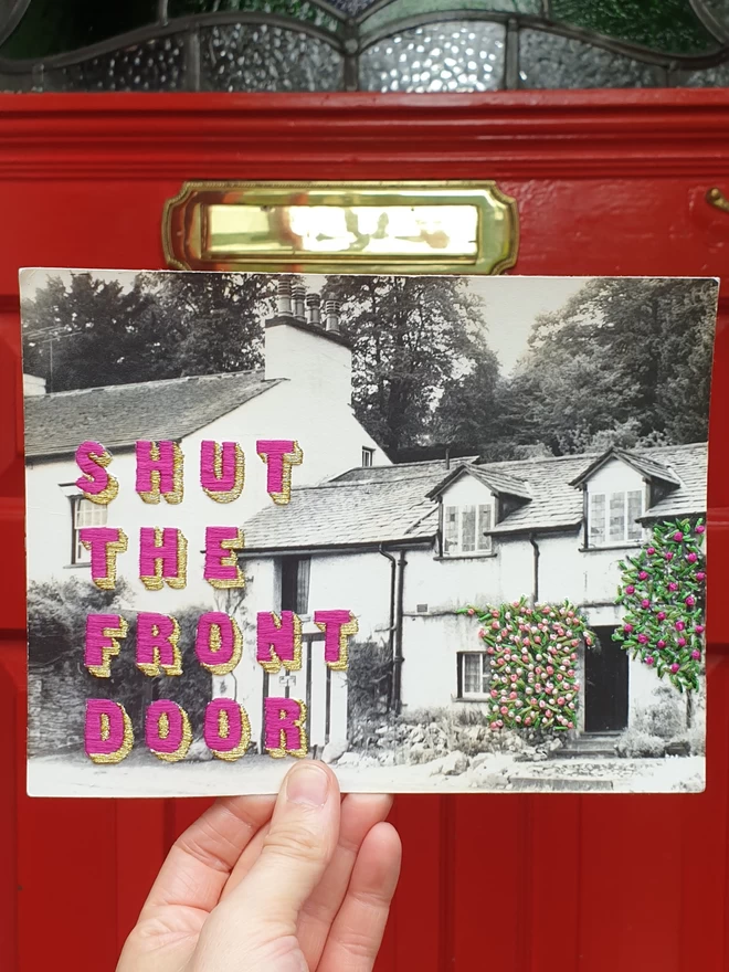  B & W photo, with embroidered "shut the front door" and florals bushes, held in front of a red door