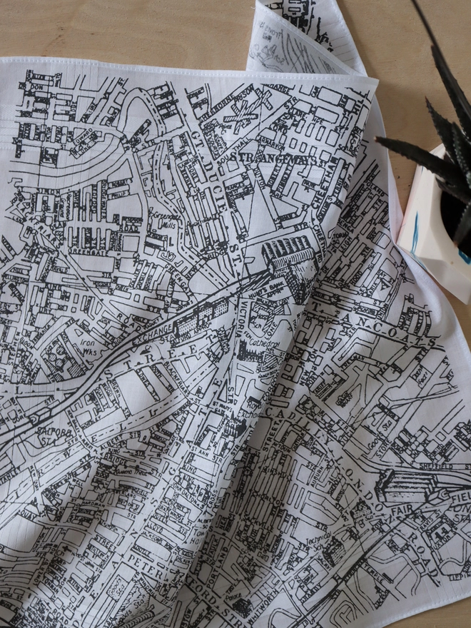 A lifestyle photo of a Mr.PS Manchester Map hankie printed in grey with a cactus in a plant pot