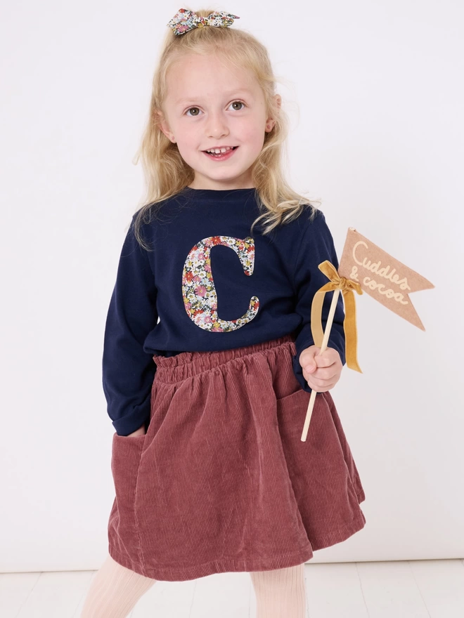 A navy cotton long sleeve t-shirt appliquéd with an initial in a floral Liberty print, worn by a 4 year old girl
