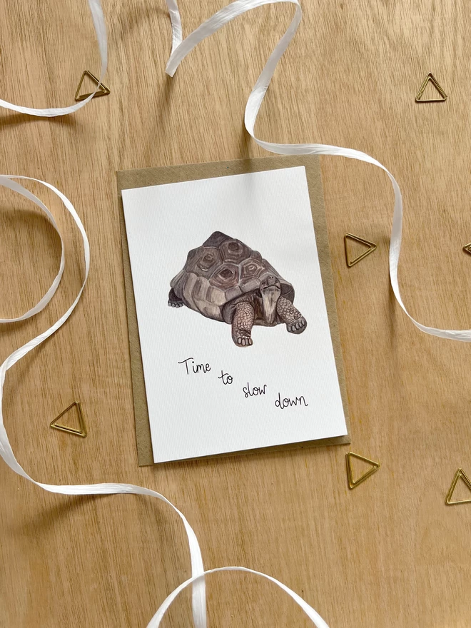a simple greetings card featuring a tortoise with the phrase “Time to slow down”