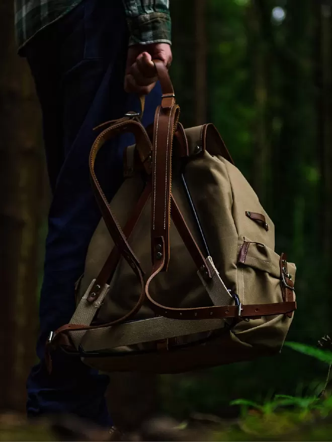 Back view showing frame of a taupe Rockness backpack held by model standing in a forest.