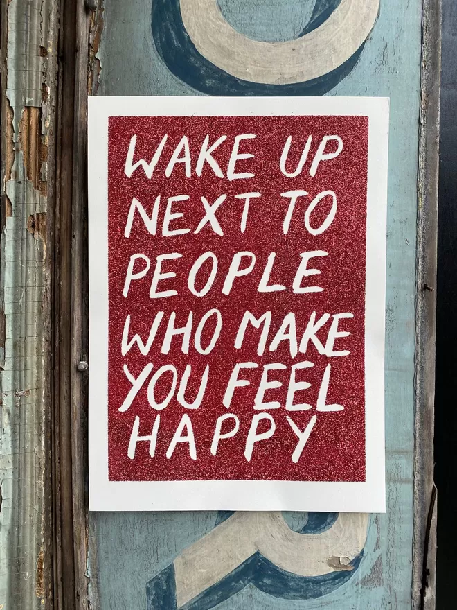 Wake up next to people who make you feel happy glitter print seen on a painted wall.