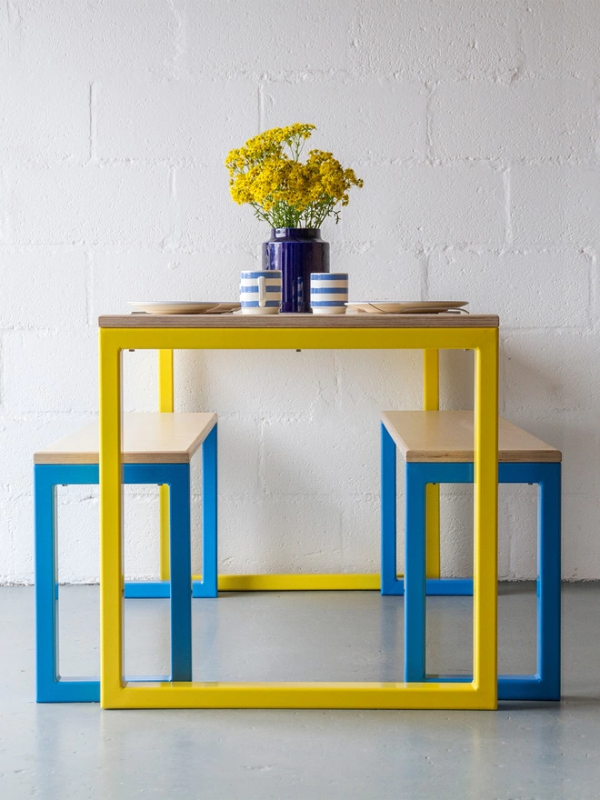 contemporary dining leg with box-section steel frames in yellow and blue, and plywood top and bench seats