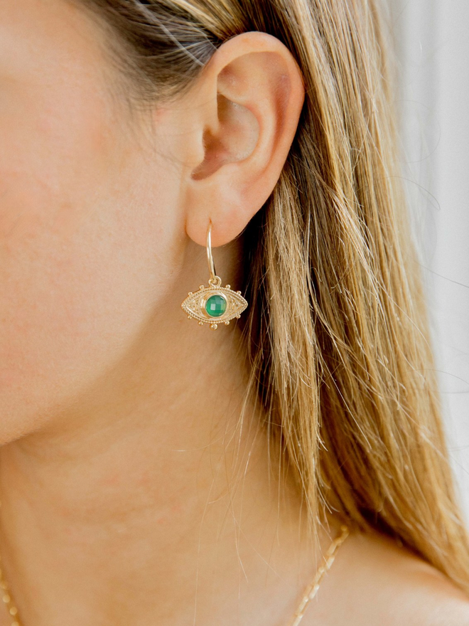 Woman wearing a small gold hoop with a green and gold evil eye charm 