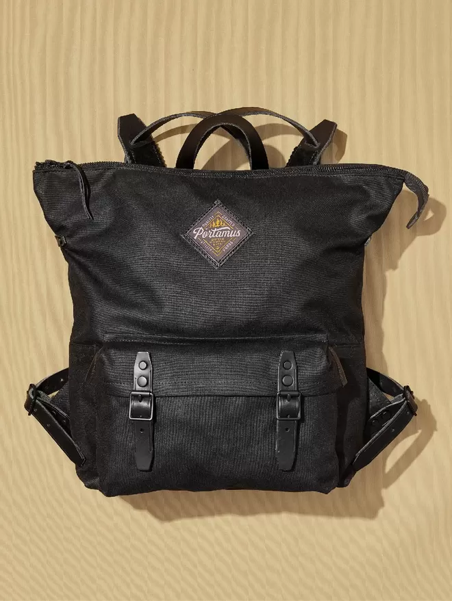 Black zip top backpack with black hardwear and black leather trim on taupe background.