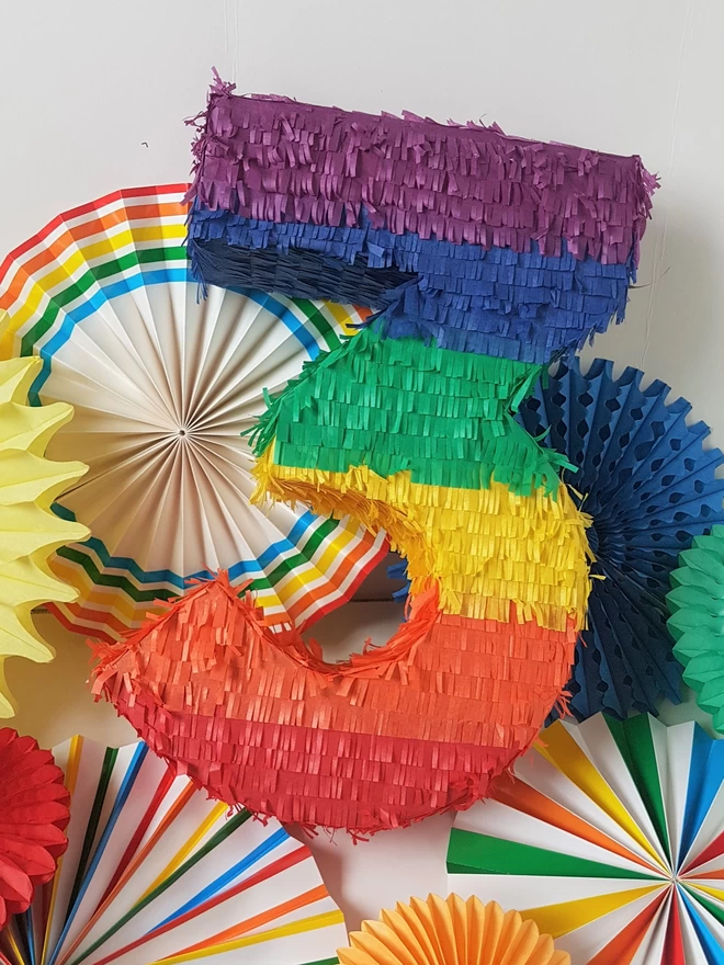 rainbow number 3 pinata on a background of rainbow paper fans