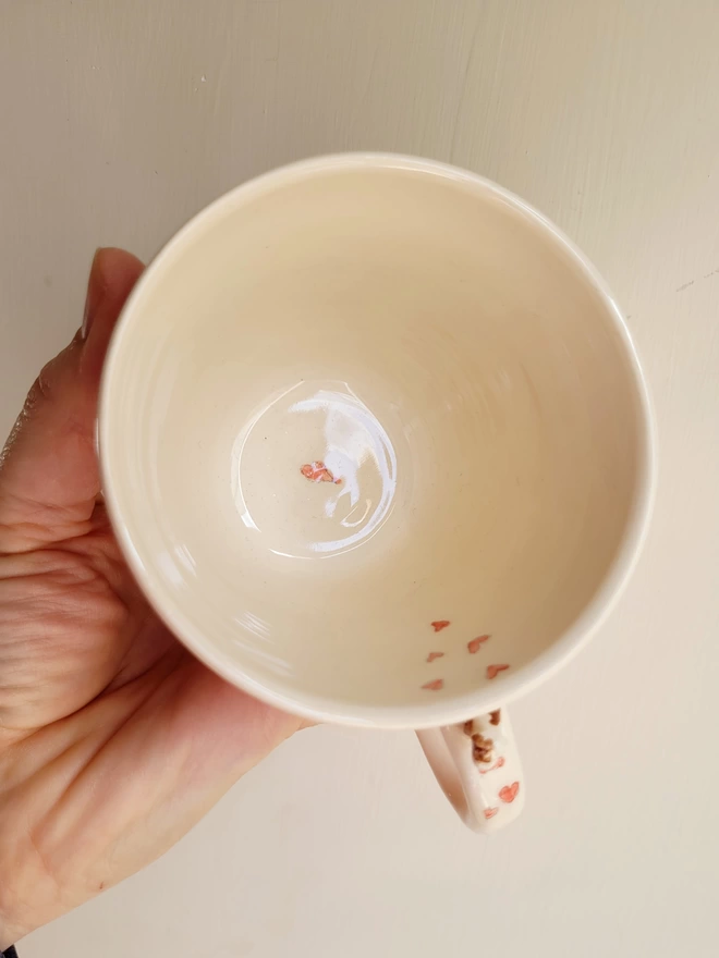the inside of a ceramic ivory white cup showing red hand painted hearts