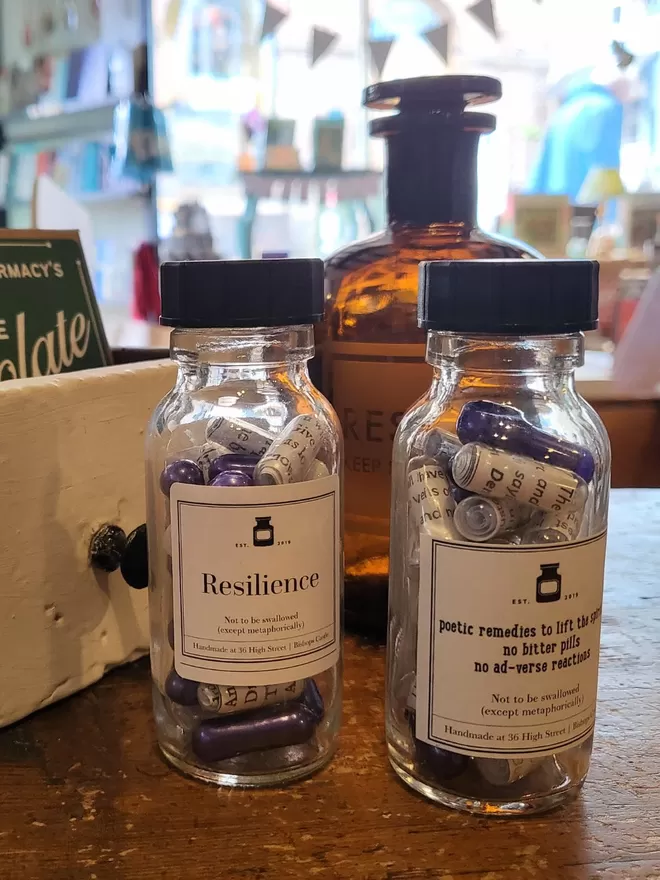 2 Glass pill bottles containing purple and clear Resilience poetry pills printed on banana paper