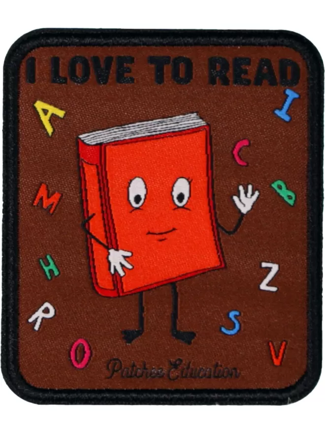 A rectangular brown patch with 'I Love To Read' at the top. In the centre is a red smiling book surrounded by colourful letters.
