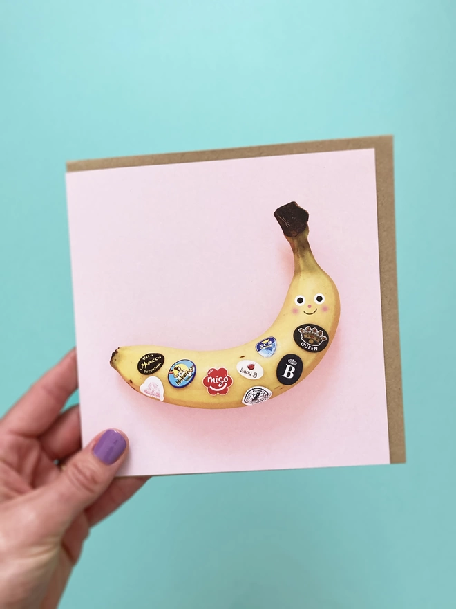 A lady holding A Pink card with a banana with fruit stickers on it