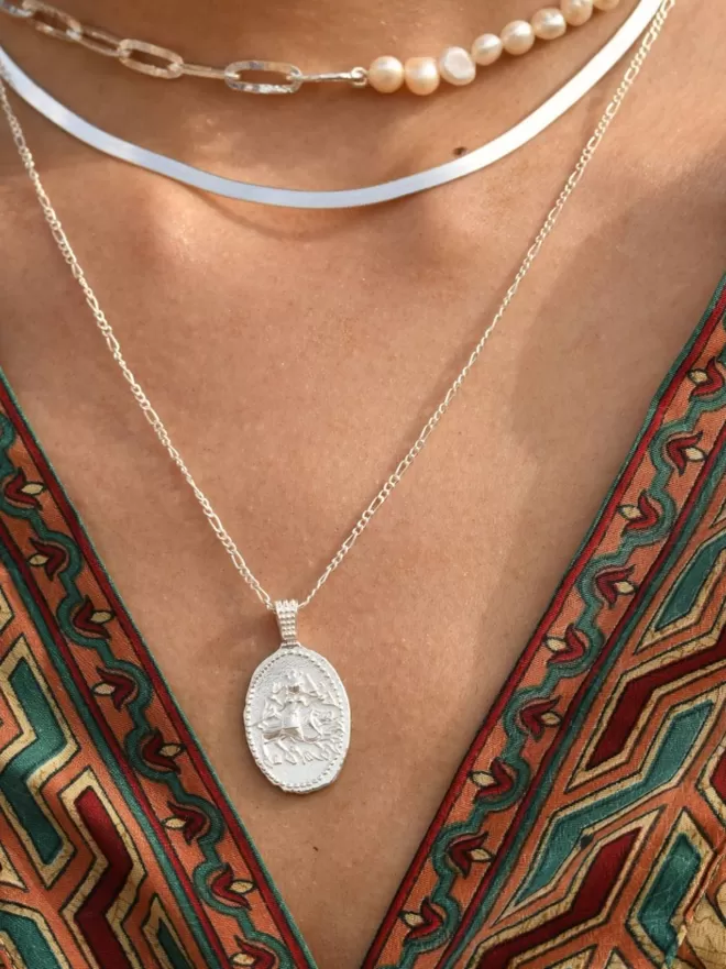 Model wears oval coin pendant with hindu goddess durga on front in silver
