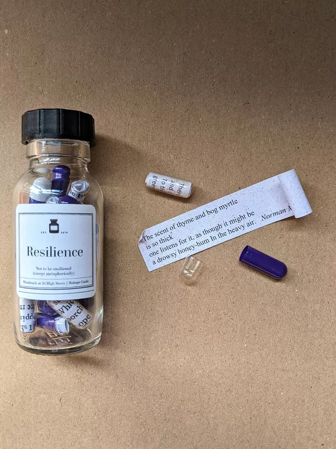 Glass pill bottle containing purple and clear Resilience poetry pills printed on banana paper