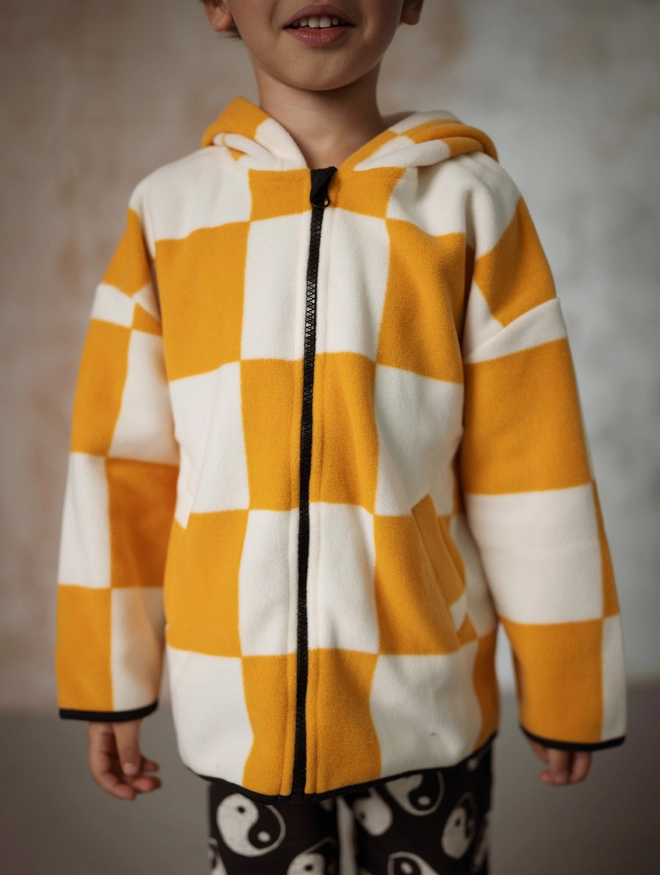 Another Fox Orange Checkerboard Polar Fleece Kids Hoody seen on a child with their arms by their side.