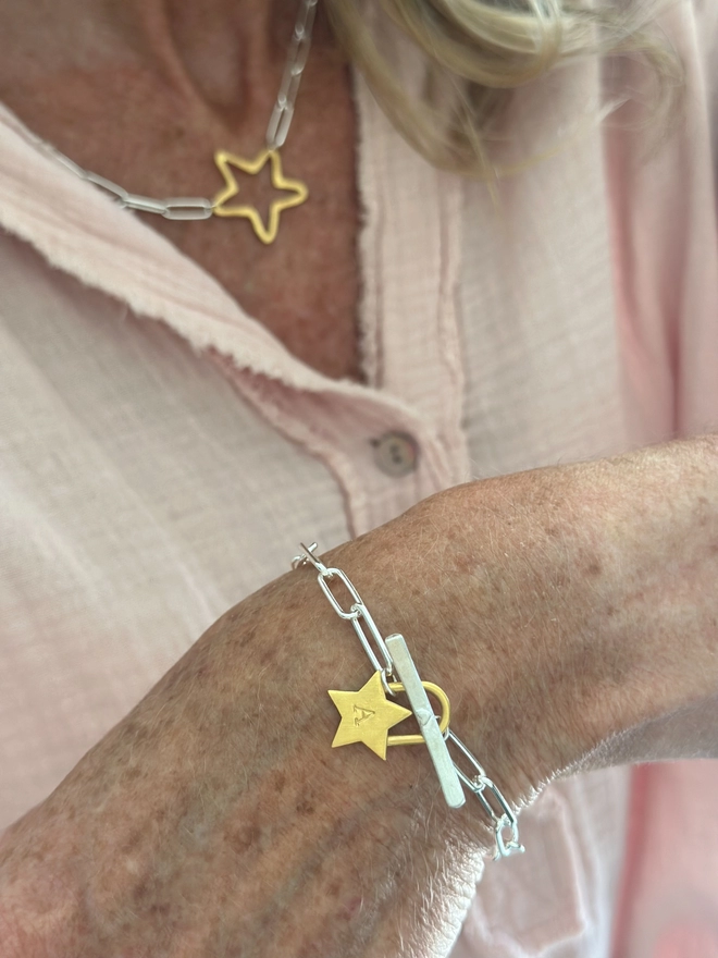 model wears a chunky gold star charm on mixed metal paperclip bracelet with T bar fastener