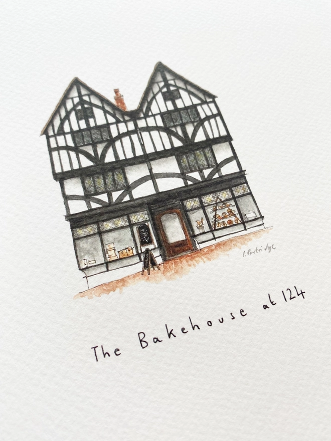 Beautiful watercolour illustration of The Bakehouse at 124, bakery in Tonbridge.  A characterful black and white tudor style three storey building with large windows on the ground floor allowing a glimpse into the bakery.The watercolour style is painted with a black pen outline and organic loose style with small details. A photo taken at an angle showing some of the detail. 