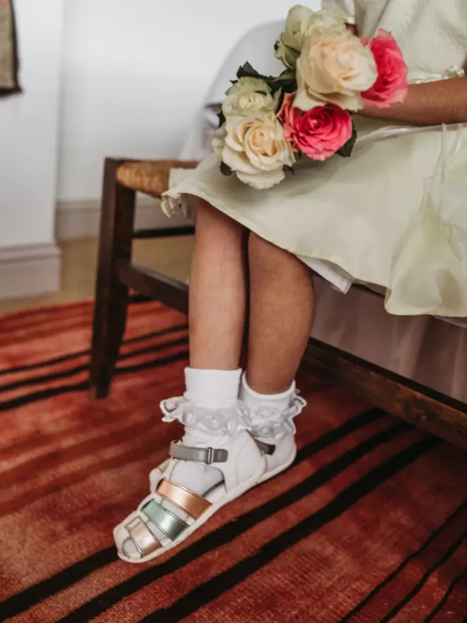 flower girl wearing Pip and Henry blue metallic gladiator sandals holding a bouquet of flowers