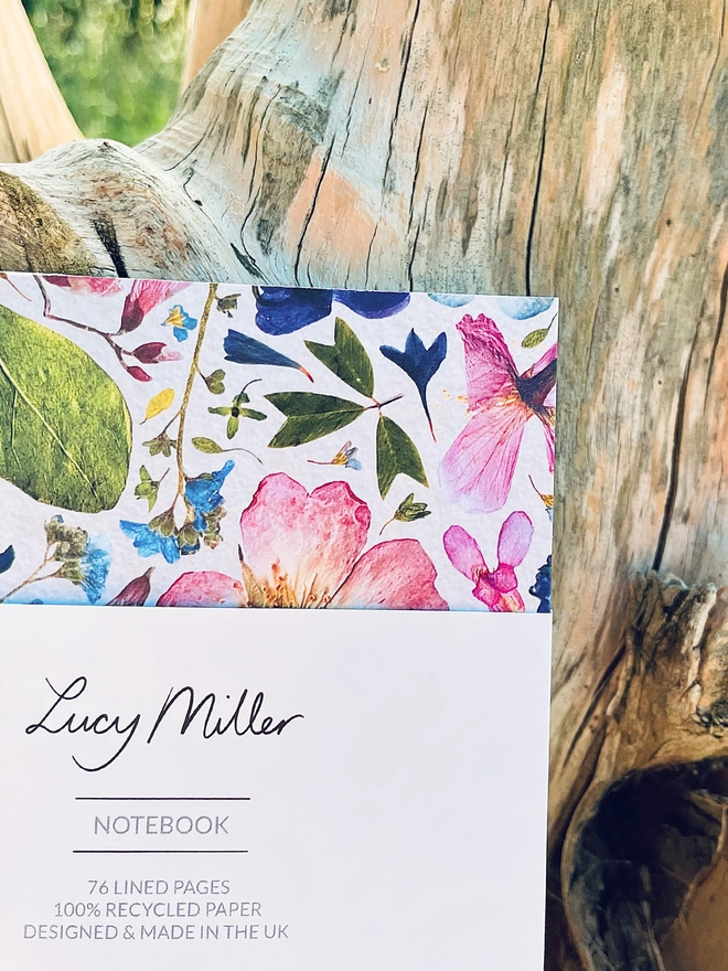 Close-up of Garden Notebook Showing Detailed Pressed Flower Print Cover, Branded Lucy Miller Belly Band, Leaning on Tree