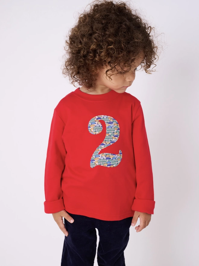 a 2 year old boy wearing a red long sleeve cotton t-shirt appliquéd with a number 2 in Liberty print featuring vintage cars 