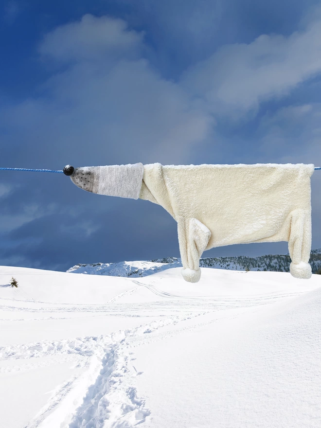Polar bear made from clothes hung on a clothes line above a snowy scene with a snow track underneath