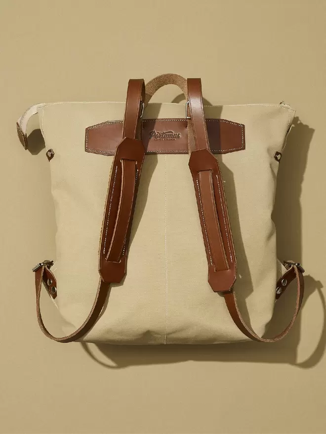 Back view of taupe backpack with brown leather trim on taupe background.