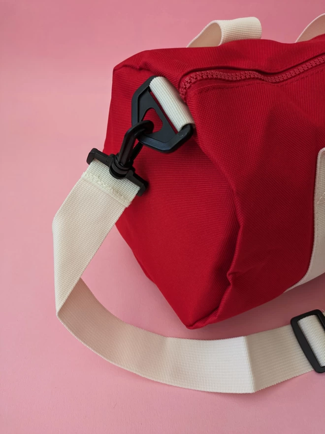 Red Duffel Bag close up detail with white straps and handles, on a pink background