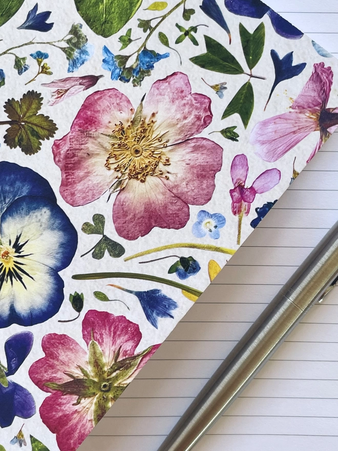 Close-Up of Wildflower Notebook Cover with Pressed Flower Design, Resting on Open Notebook with Ruled Pages