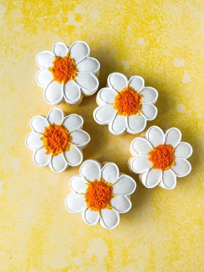 five large daisy macarons decorated with white icing on a yellow background