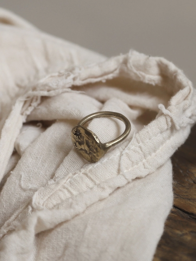 Image of a gold toned brass ring with the image of a horse and star on it laying on a piece of cream linen fabric on top of a rustic piece of wood