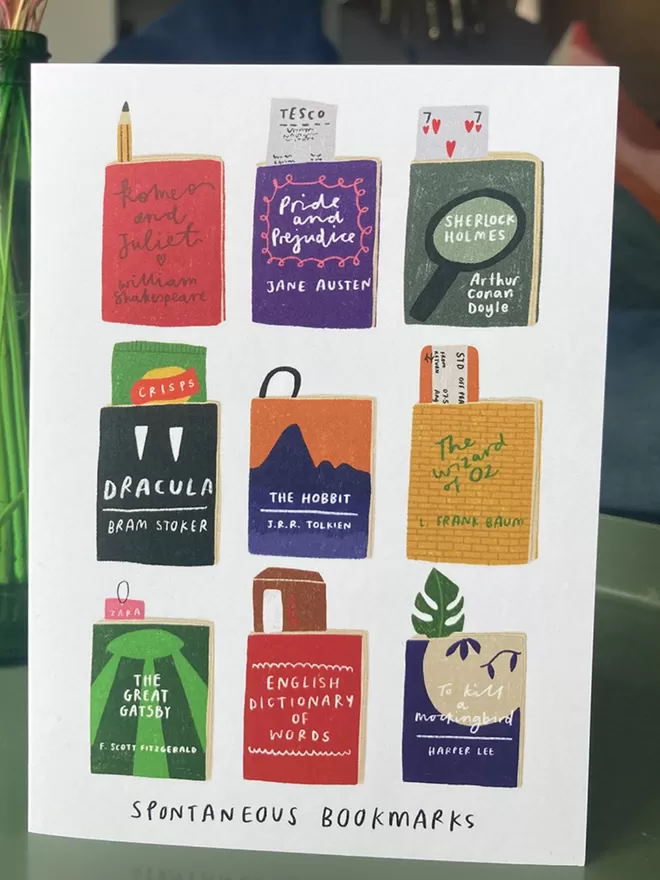 Greetings card with images of books and random bookmarks. Placed on a table with flowers in the background
