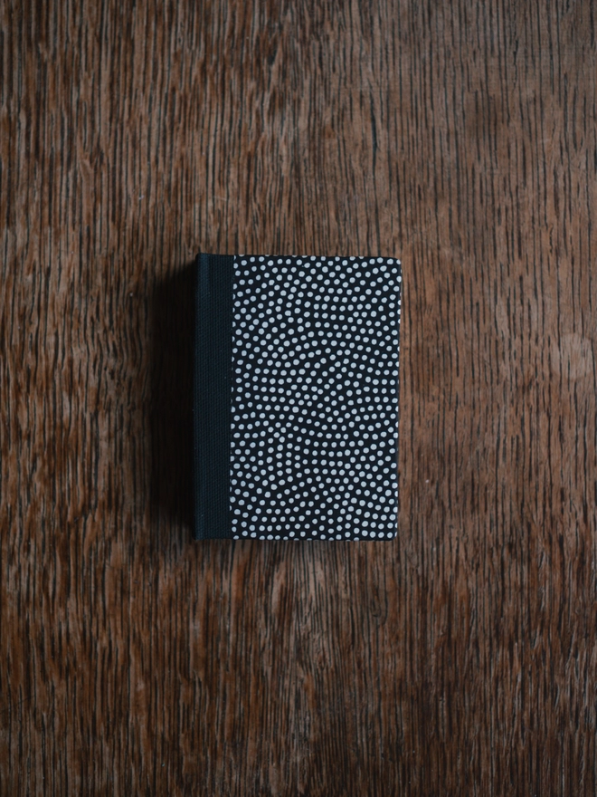 Miniature book with a black cover with white dots and black cloth spine
