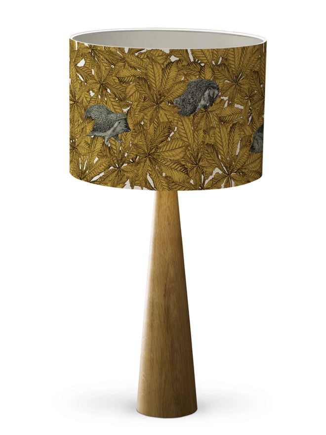 Drum Lampshade featuring hedgehogs in yellow autumn leaves with a white inner on a wooden base on a white background