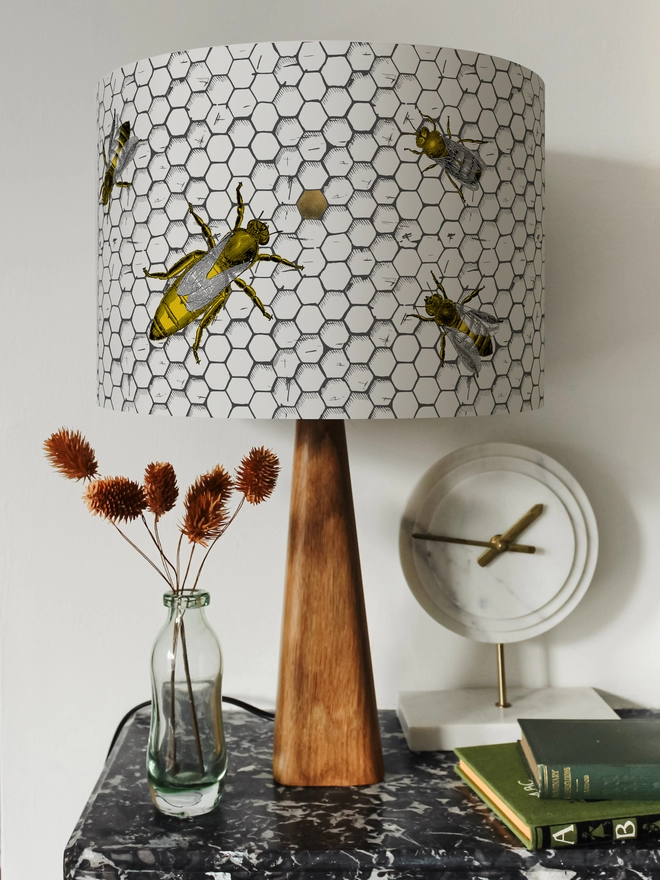 Drum Lampshade featuring honey bees on a honeycomb on a wooden base on a shelf with books and ornaments