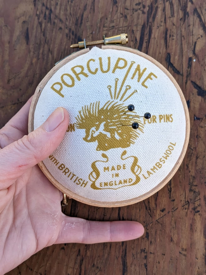 Hand holding a mustard coloured porcupine embroidery hoop pin cushion