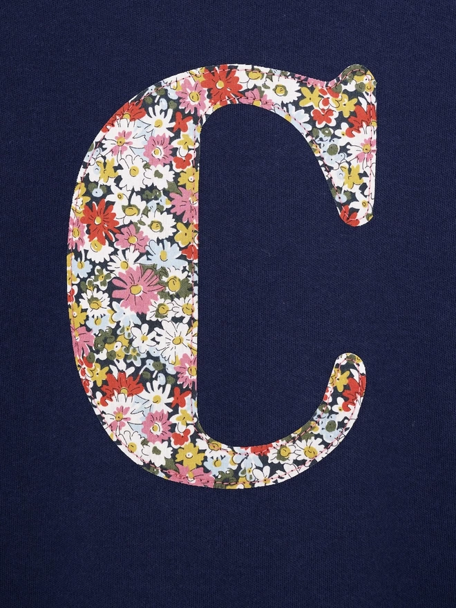 A navy cotton long sleeve t-shirt appliquéd with an initial in a floral Liberty print, a close up of the stitching