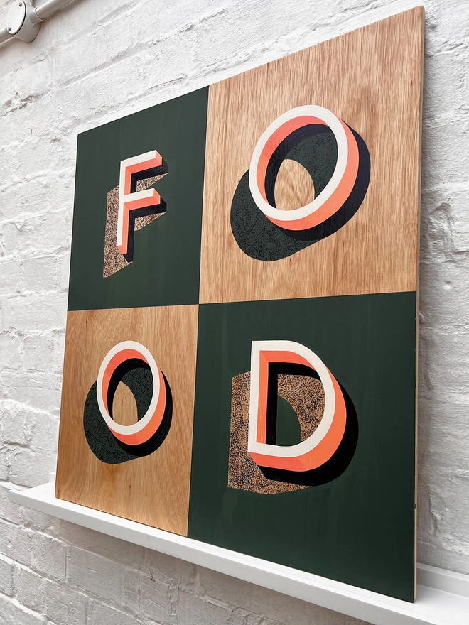 FOOD hand painted sign in coral, green and aubergine, against a white brick wall, at an angle. 