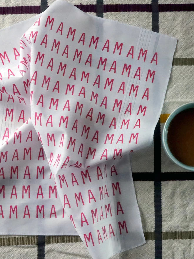 A Mr.PS MAMA hankie laid on a checked tablecloth alongside a cup of tea