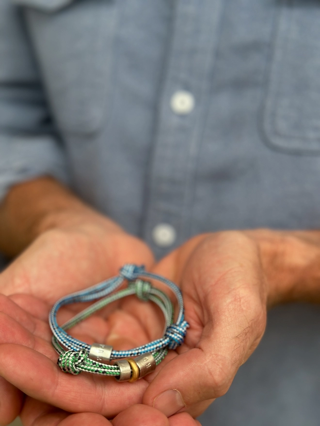 model holds men's personalised sterling silver bead friendship bracelets. one on blue, the other on green cord