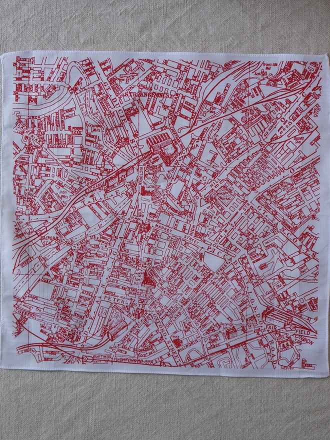 A Mr.PS Manchester map hankie printed in red laid flat on a linen tablecloth