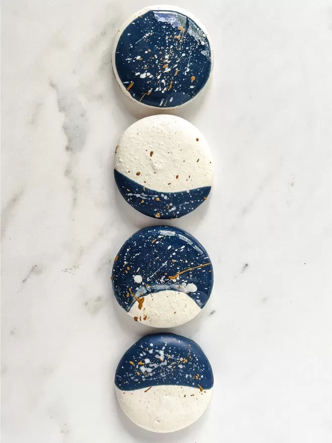 four moon macarons in different moon phases with deep blue starry night with gold & white speckles sitting on top of a marble surface