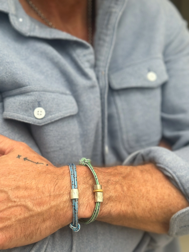 model wears two men's personalised sterling silver bead friendship bracelets. one on blue cord, the other on green